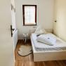 Gemütliche Zimmer im Altbau, © Kloster NaturSinne Ein kleines, gemütliches Schlafzimmer mit einem Einzelbett, Holzboden und einem kleinen Fenster mit Jalousie.