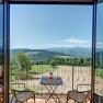 View from the room, © Wachahof View from a balcony of a hilly landscape with forests and fields, two chairs and a table with flowers in the foreground.