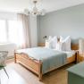 Schlafzimmer Feriennest Zehetbauer, © heiter-weiter.at/Karl Stangl Ein gemütliches Schlafzimmer mit einem Holzbett, blauer Bettdecke, Nachttischen und einem Schreibtisch mit Stuhl. Helle Vorhänge und ein Fenster sind zu sehen.