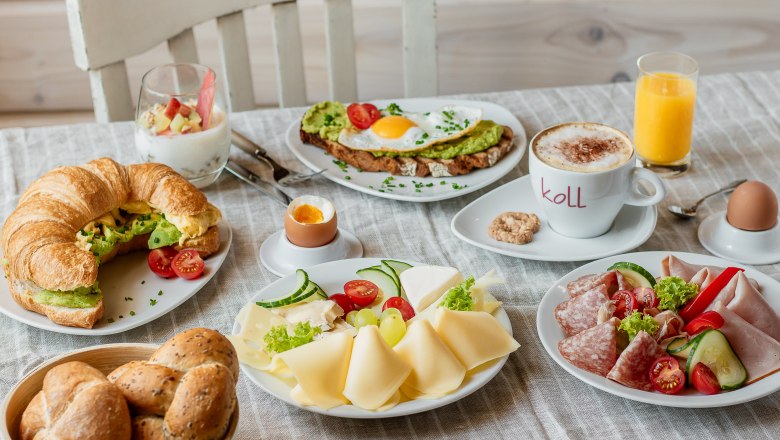 Frühstück, © Koll GmbH Ein reichhaltiges Frühstück mit Croissant, Brötchen, Käse, Aufschnitt, Avocado-Toast, Joghurt, Cappuccino, Orangensaft und weichgekochtem Ei.
