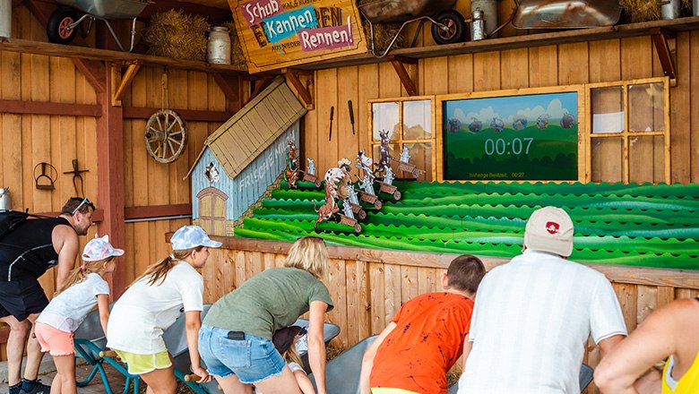 Eis-Greissler adventure park wheelbarrow race, © Blochberger Eisproduktion GmbH Children and adults in front of the "wheelbarrow race" attraction in an adventure park.