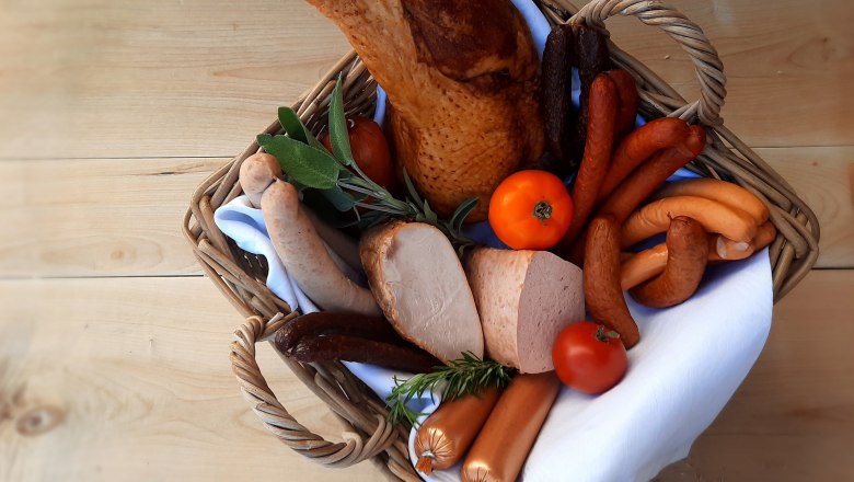 Sausage products from the organic turkey, © Biohof Puchegger Various sausage products from the organic turkey in a basket with herbs and tomatoes on a wooden table.