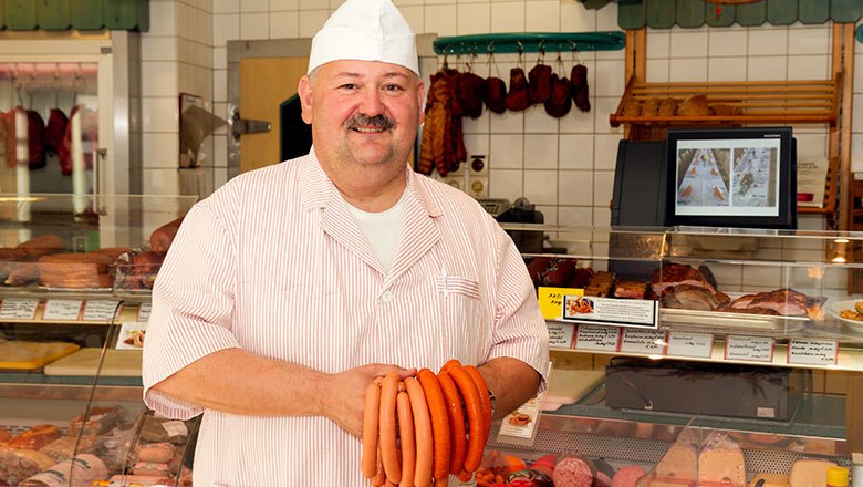 Franz Pürrer, © Sooo gut schmeckt die Bucklige Welt/ Viktoria Kornfeld A man dressed in white holds sausages in a butcher's store.