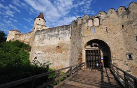 Burg Seebenstein, © POV Eingangstor einer alten Burg mit Holztor und Zinnenmauer, blauer Himmel im Hintergrund.