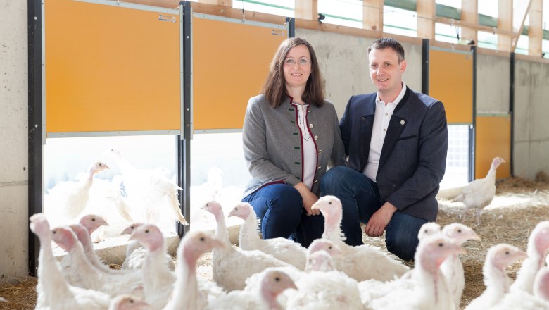 Organic turkey family Puchegger, © LK NÖ, Gerald Lechner A woman and a man kneel in a barn with many white turkeys.