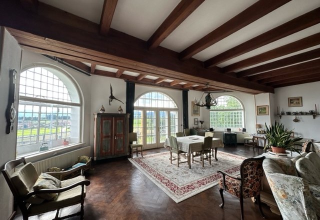 Schloss Gut Ziegersberg, © Schloss Gut Ziegersberg Ein elegantes Wohnzimmer mit Holzbalkendecke, großen Fenstern, antiken Möbeln und einem Teppich.