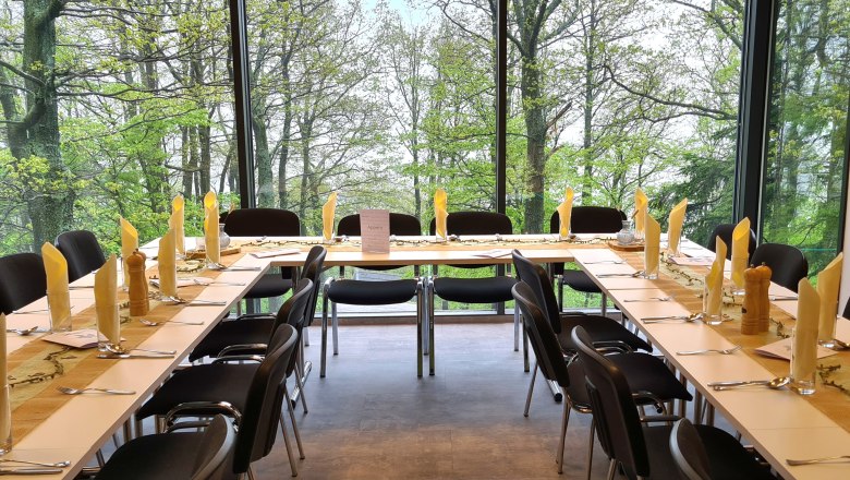 Feiern im Turmcafé, © Gemeinde Schwarzenbach Gedeckte Tische mit gelber Dekoration und schwarze Stühle vor einer großen Fensterfront mit Ausblick auf Bäume.