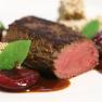 Köstliches aus der Haubenküche, © Familie Görg Gourmetgericht mit rosa gebratenem Fleisch, Obst und Kräutern auf einem weißen Teller angerichtet.