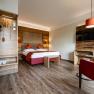 The guest house in the Triad, © Marketing Platzhirsch, Gobauer Modern hotel room with double bed, wooden furniture and red armchair.