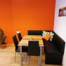 Breakfast room, © Pension zum Spitz A modern breakfast room with an orange wall, black corner bench, table and chairs. A plant stands in the corner, a picture hangs on the wall.