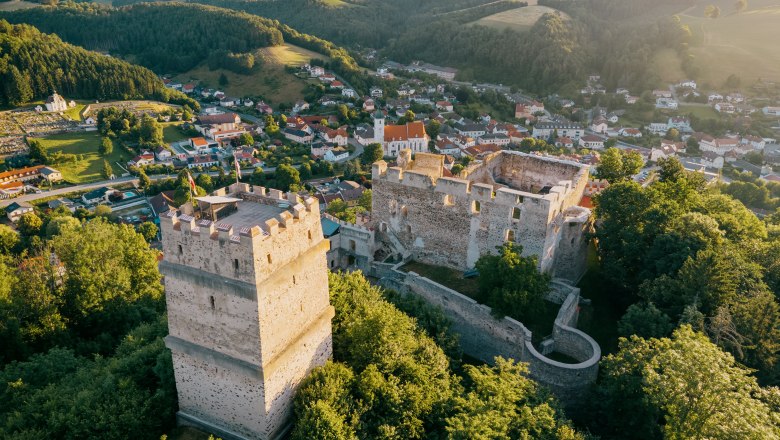 Aerial view with fire tower, castle ruins and the village of Kirchschlag, © Wiener Alpen, Roman Königshofer Aerial view of the ruins of Kirchschlag Castle surrounded by green trees and the municipality of Kirchschlag in the background.