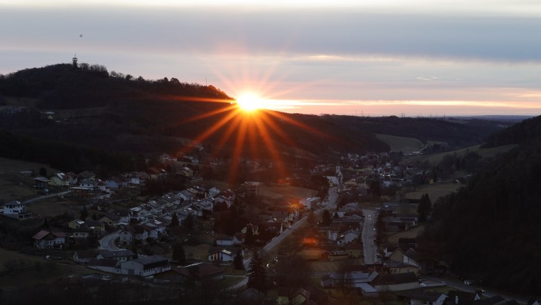 Sonnenaufgang hinterm Keltenberg, © Marktgemeinde Schwarzenbach, Helmut Karner Sonnenaufgang hinter einem Hügel mit einem Dorf im Vordergrund.