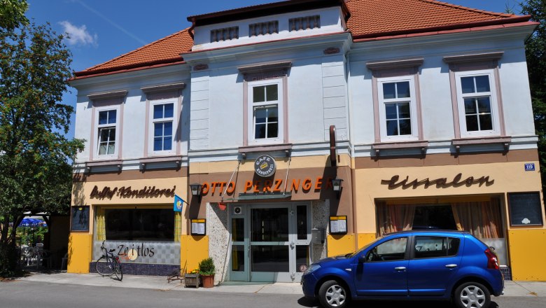 Zeitlos aussen, © Thermengemeinden Außenansicht eines Cafés mit blauer Fassade und rotem Dach, davor ein blaues Auto geparkt.