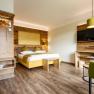 The guest house in the Triad, © Marketing Platzhirsch, Gobauer Modern hotel room with wooden furniture, double bed, green armchair and flat screen TV.