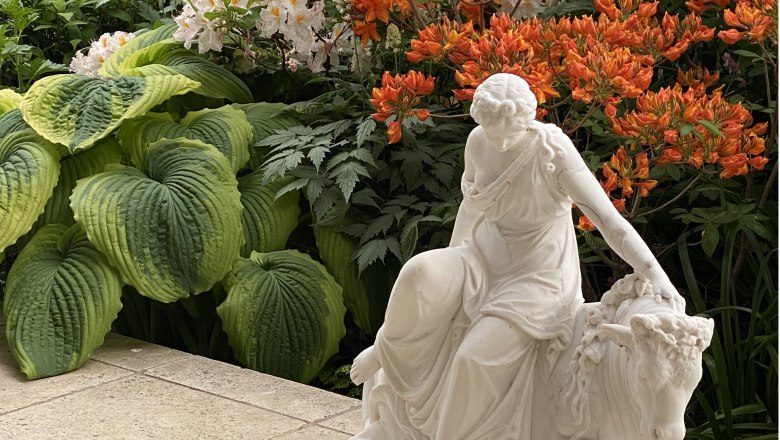 Fernery - Glass house in the Ecolution.Lab, © Bernd Hochwartner White statue of a woman next to large green leaves and orange flowers.