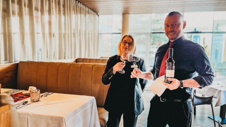 Das Linsberg - Restaurantteam, © Linsberg Asia Zwei Personen in einem Restaurant stoßen mit Weingläsern an, eine Person hält eine Weinflasche.