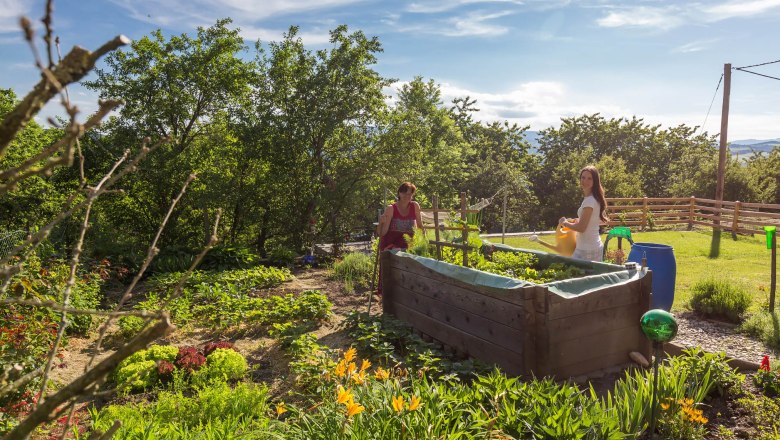 Gardening, © Wachahof Two people work in a sunny garden with raised beds and plants.