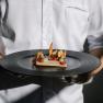 Haubenküche im Restaurant Görg, © Wiener Alpen, Sophie Menegaldo Person im weißen Hemd hält einen Teller mit einem kunstvoll angerichteten Gourmetgericht.