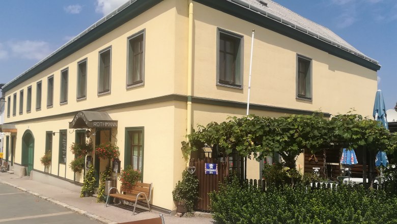 Gasthaus zur Gemütlichkeit Hochwolkersdorf, © Wiener Alpen Gelbes Gasthaus mit grünen Fensterrahmen, Gastgarten und Pflanzen vor dem Eingang.