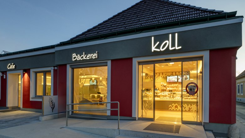 Bakery Koll, © Michaela Begsteiger, Koll GmbH Exterior view of the bakery in the evening with illuminated sign 'Bäckerei Koll' and 'Cafe'.