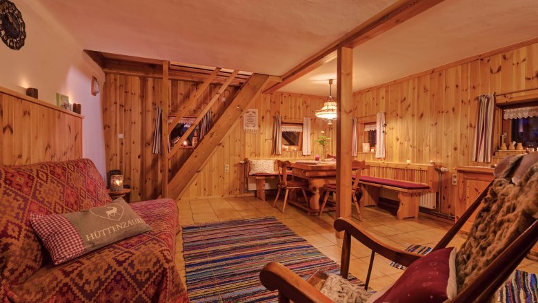 Living-dining room, © Wachahof Cozy living room with wooden walls, sofa, rocking chair and dining table. Rustic ambience with carpet and warm light.