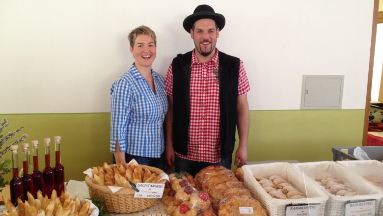 Market stall, © Fam. Luckerbauer Two people are standing in front of a market stall with fresh pastries and bottles.