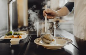 Wirtshausspezialitäten aus dem Suppentopf, © Niederösterreich Werbung/Sophie Menegaldo Eine Person schöpft Suppe mit einem Knödel aus einem Topf in einen Teller.