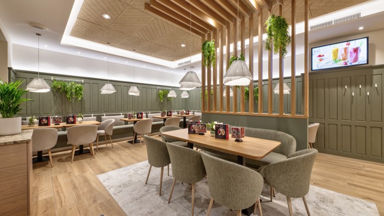 Café-Bakery Koll, © Michaela Begsteiger, Koll GmbH Interior view of the modern café with wooden tables, upholstered chairs and hanging plants.