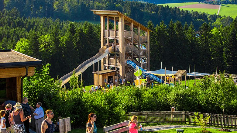 Eis-Greissler adventure park slide tower, © Blochberger Eisproduktion GmbH Wooden slide tower surrounded by trees, and people in the foreground.