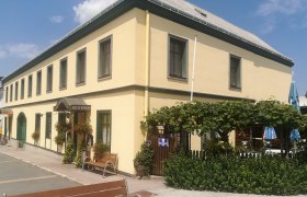 Gasthaus zur Gemütlichkeit Hochwolkersdorf, © Wiener Alpen Gelbes Gasthaus mit grünen Fensterrahmen, Gastgarten und Pflanzen vor dem Eingang.