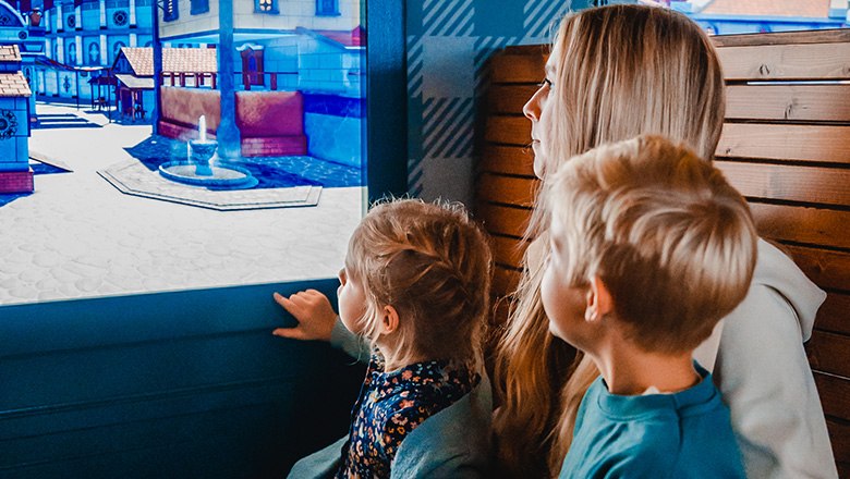 Eis-Greissler ice cream time travel express train inside, © Blochberger Eisproduktion GmbH Two children and a woman look out of the window of a train at a virtual city.
