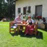 A warm welcome, © Wachahof Two people are sitting at a wooden table in the garden in front of a house with flowers.