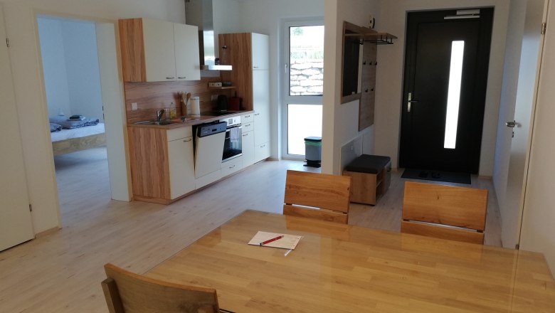 Wohnküche, © Peter Hecht Moderne Wohnküche mit Holzmöbeln, Esstisch, Küchenzeile und Eingangstür.