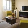 Appartment Wohnbereich, © Vitalzeit Hotel Weber Moderner Wohnbereich mit Sofa, grünem Sessel, Couchtisch, Kamin und Fernseher.