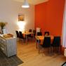 Breakfast room, © Pension zum Spitz A breakfast room with two tables, black chairs and orange tablecloths. A chest of drawers with a coffee machine is on the left.