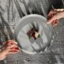 Regionale 3 Haubenküche im Restaurant Görg, © Wiener Alpen, Sophie Menegaldo Zwei Hände halten ein Teller mit einem kunstvoll angerichteten Gourmetgericht über einem Holztisch.