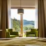 The guest house in the Triad, © Marketing Platzhirsch, Gobauer Interior view of a guest room with two green armchairs in front of a large window overlooking a hilly landscape.