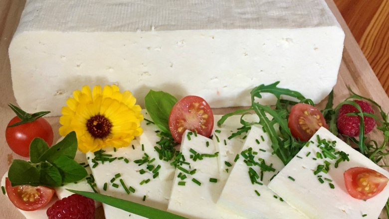 Schafkäse vom Bio-Schafbauernhof Kölbel, © Kölbel Ein Block Schafkäse in Scheiben geschnittenen, garniert mit Tomaten, Himbeeren, Rucola und einer gelben Blume auf einem Holzbrett.