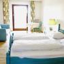 Großes Zimmer, © Seminarhotel NaturSinne Ein helles Zimmer mit einem Doppelbett, blauer Couch, Tisch und Stuhl vor einem Fenster mit Vorhängen.