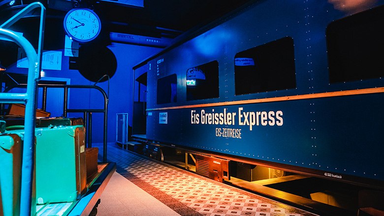 Eis-Greissler ice cream time travel express train, © Blochberger Eisproduktion GmbH A wagon of the Ice Time Journey in a darkened room, next to it a baggage car.