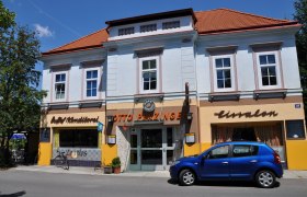 Zeitlos aussen, © Thermengemeinden Außenansicht eines Cafés mit blauer Fassade und rotem Dach, davor ein blaues Auto geparkt.