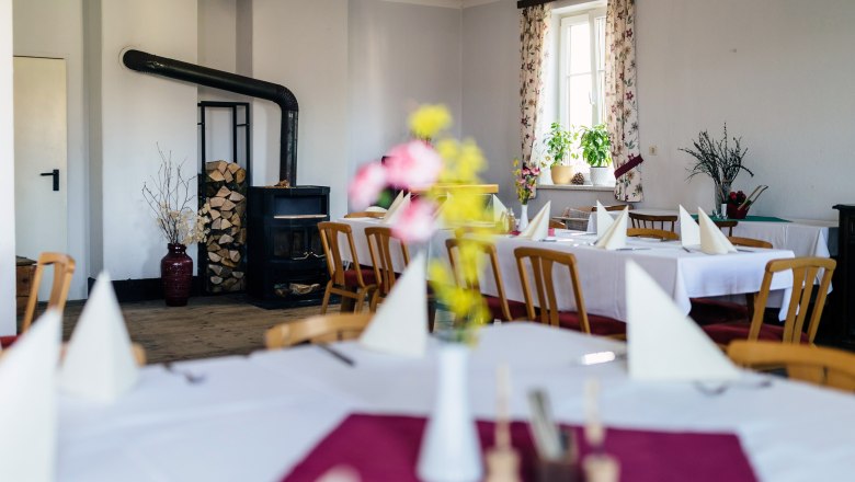 Hall in the Gasthaus der Kräuterwirtin, © Nicole Heiling Cozy guest room with wood-burning stove, laid tables and flowers.