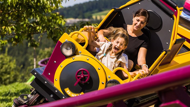 Eis-Greissler adventure park Bucklbahn, © Blochberger Eisproduktion GmbH A woman and a child in the carriage of a roller coaster in the Eis-Greissler adventure park.