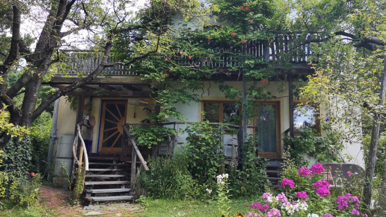 Forest garden at the Rosalia, © "Natur im Garten" A house with a wooden balcony, surrounded by trees and colorful flowers in the garden.