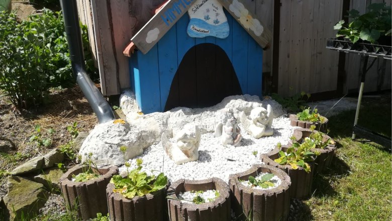 Natural garden paradise Beisteiner - "Himmelsschlüsserl", © Wiener Alpen Small blue house with angel figures and plants in a garden.