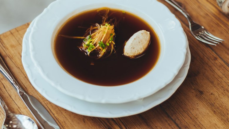Klare Rindssuppe mit Einlagenvariation, © Niederösterreich Werbung/David Schreiber Eine klare Rindssuppe mit Gemüse und Knödel in einem weißen Teller auf einem Holztisch.