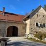 Tailor's goods, © Wiener Alpen Old stone building with red tiled roof and wooden gate, surrounded by paved path and vegetation.