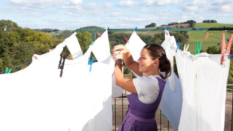 Gasthof zum Stickelberg, © Korntheuer Woman hangs laundry outdoors, with rural landscape in the background.