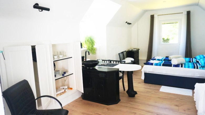 Ferienhaus Innenansicht, © Maria Theresia Schwarz-Mach Innenansicht eines hellen Ferienhauses mit Bett, Tisch, Stühlen und Küchenzeile.