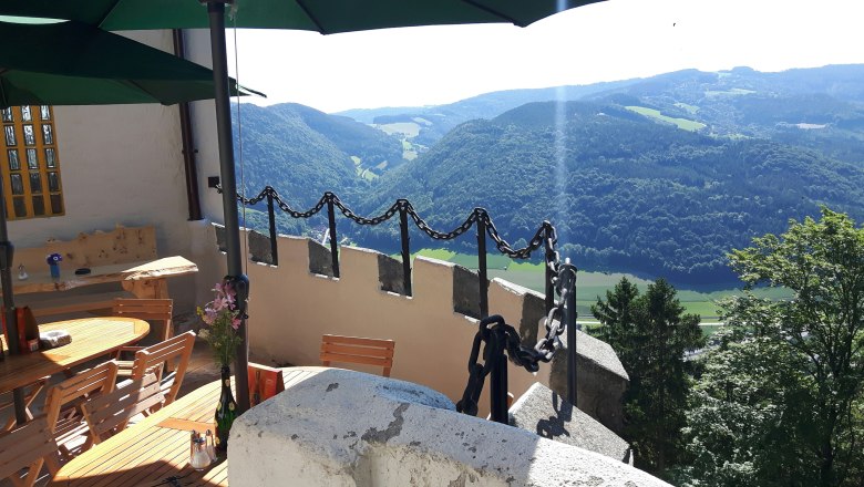 Wonderful view from the terrace, © www.burg-grimmenstein.at Terrace with wooden tables and chairs, view of wooded hills and valley.